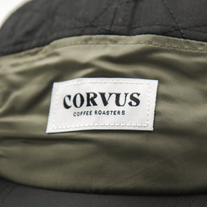 Detail of patch on five-panel hat depicting logo for Corvus Coffee Roasters.