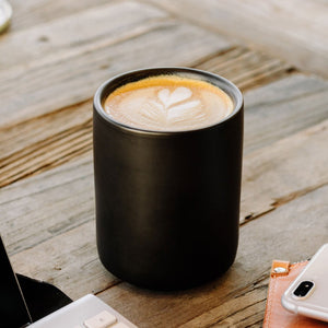 Matte black ceramic coffee mug from Fellow, on a table surface with latte art.