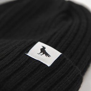 Detail of a black wool beanie with a tag depicting a crow.