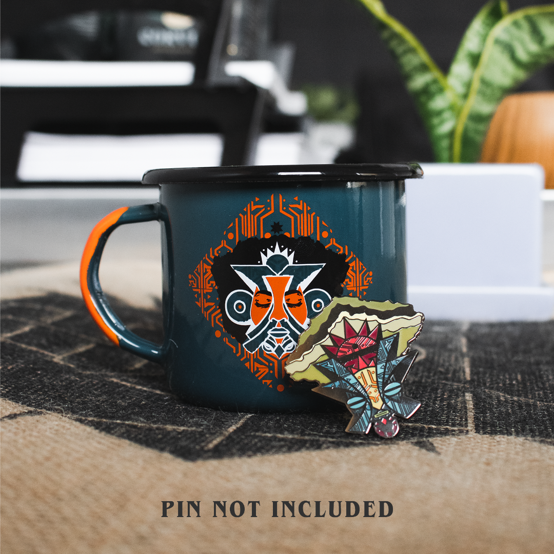 Enamel pin propped up against a metal coffee mug with coordinating designs of an African mask.