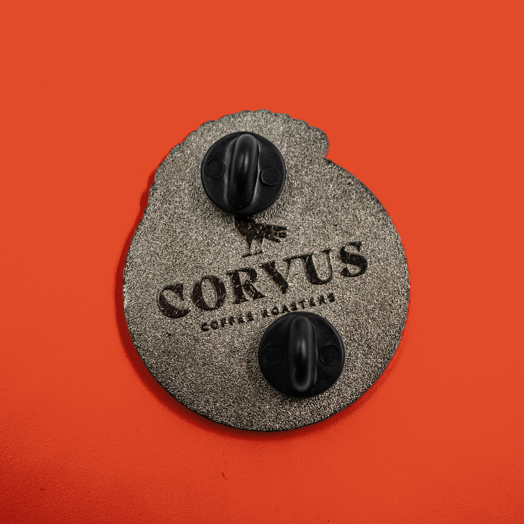 Details of backside of enamel pin showing pinbacks and Corvus Coffee Roasters logo.