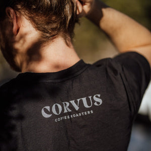 Person wearing a t-shirt with detail of back of shirt depicting Corvus Coffee Roasters logo.