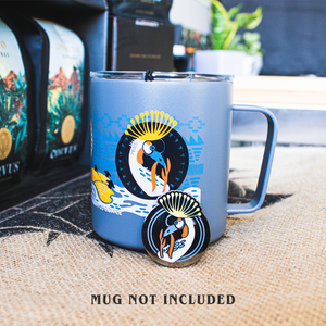 Enamel pin propped up against a metal coffee mug with coordinating designs of crowned crane.