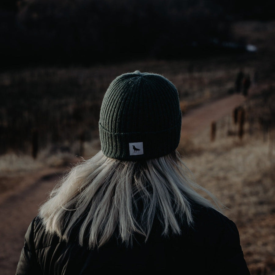 Green knit wool beanie with a tag depicting a crow.