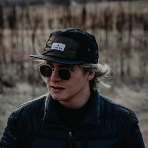 Person wearing a five panel hat outside in wilderness setting.