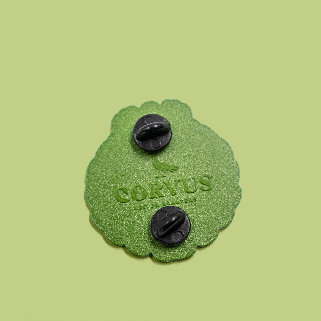 Details of back of enamel pin, showing pinbacks and Corvus Coffee Roasters logo.