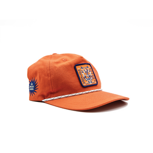Orange baseball hat designed by Charlie Wagers depicting a traditional central american mask.